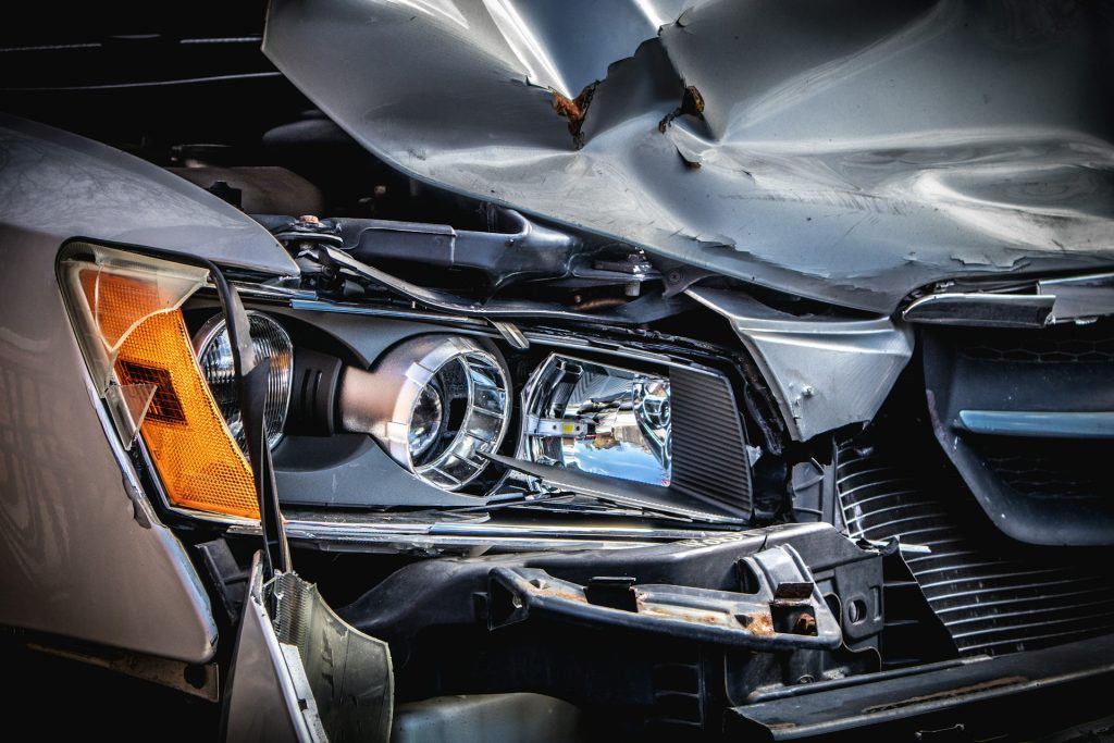 Close-up of a grey car’s crumpled front bumper and broken headlight after a collision