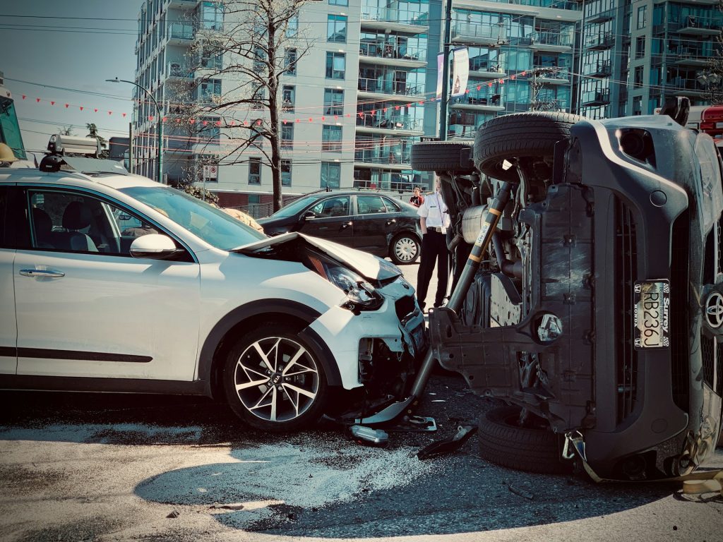 A white SUV with front-end damage next to an overturned vehicle at an urban accident scene