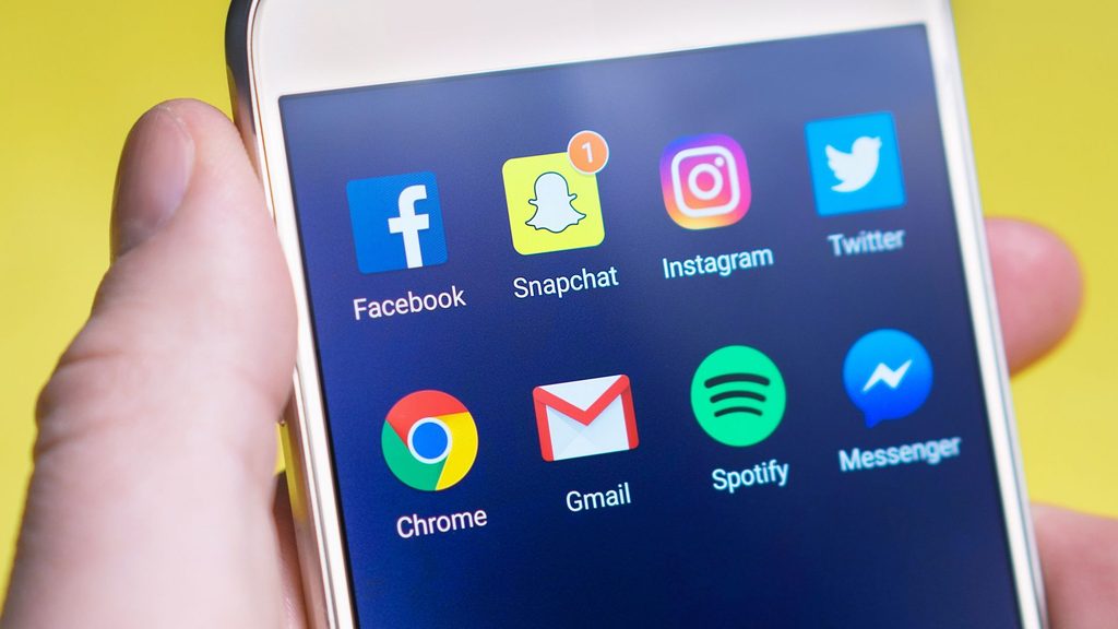 A hand holding a smartphone with a screen showing social media app icons